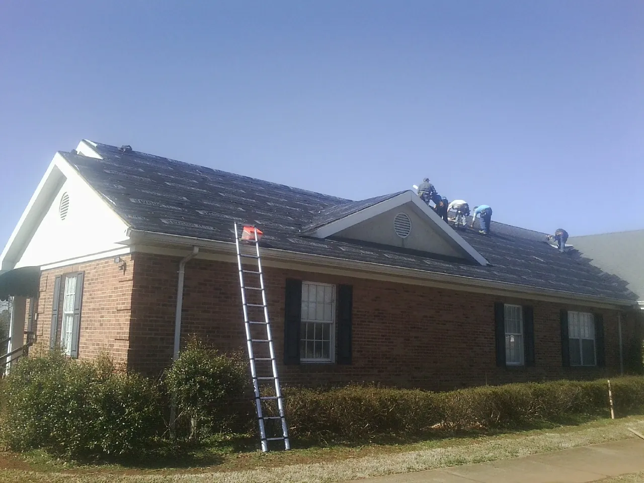 Crew tearing shingles off a brick ranch roof with a ladder set — Emergency Roof Repair work by our crew in Mount Aetna