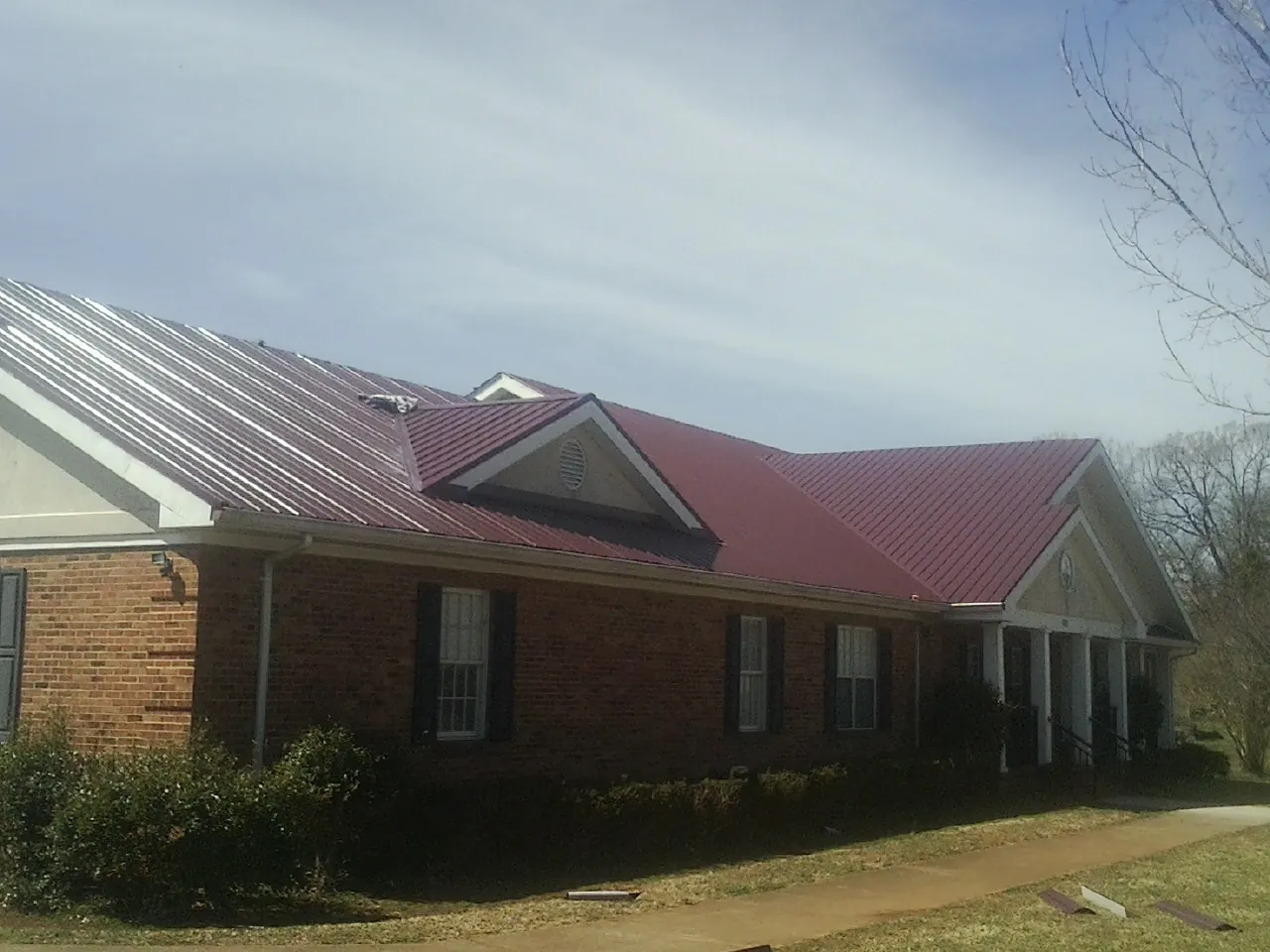 Red metal roof with gabled entries on a long brick building, from a Hail Damage Roof Repair job in Mount Aetna