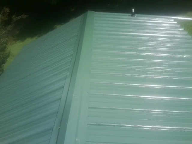 New green metal panels meeting at the ridge of a roof — Flat Roof Repair work by our crew in Mount Aetna