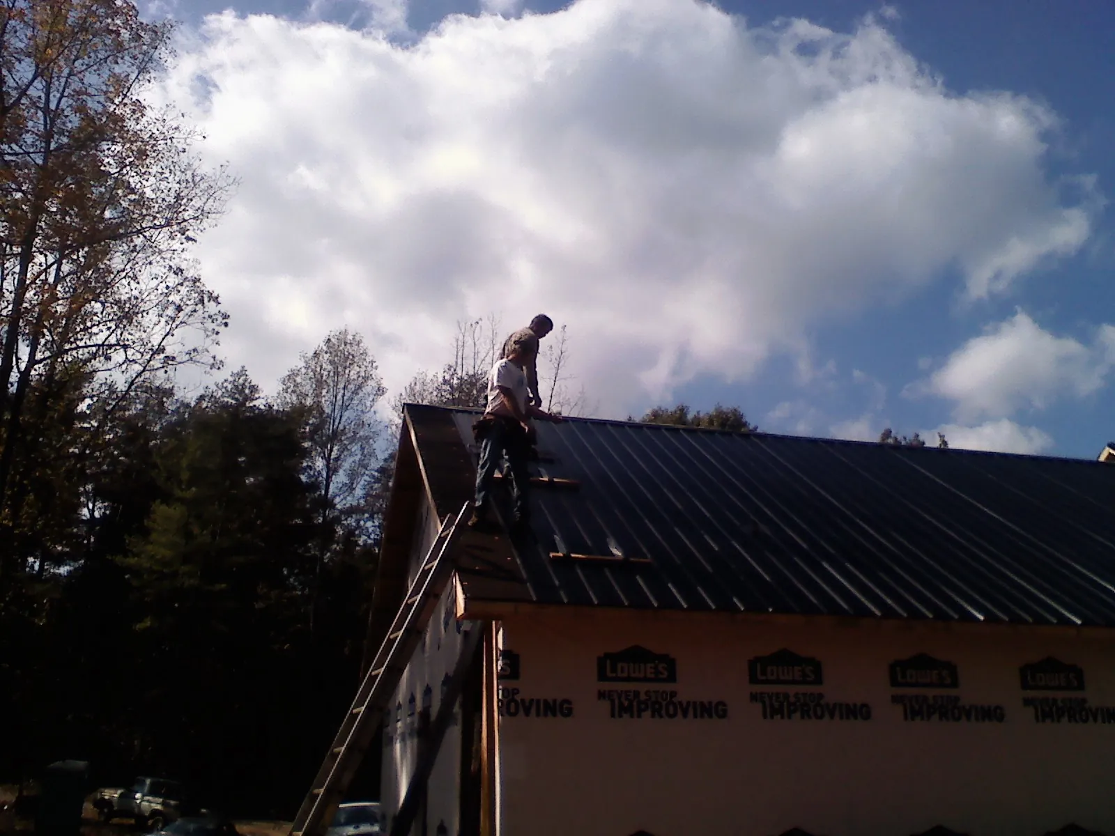 Roofer fastening dark metal panels high against a cloudy sky, from a Roof Inspection job in Mount Aetna