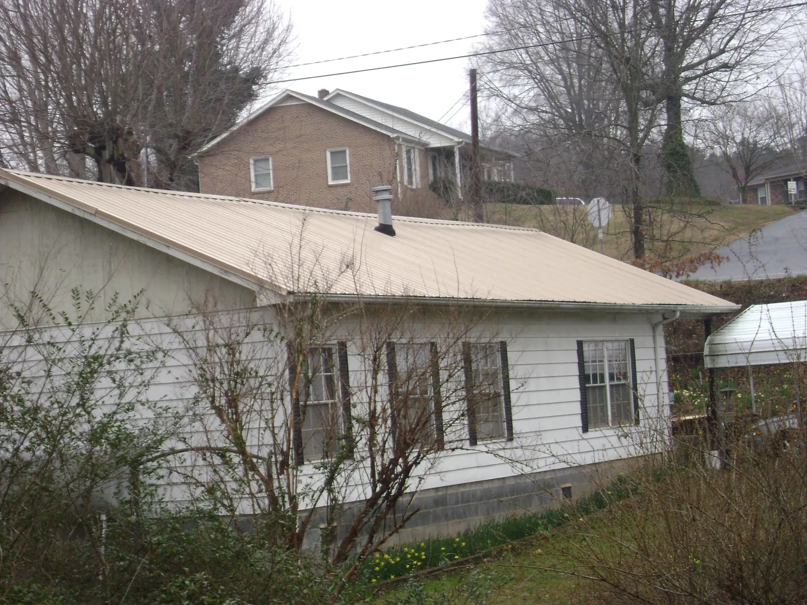 Tan metal roof on a white sided house set into a hillside — Commercial Roofing by Roofing Brothers in Mount Aetna
