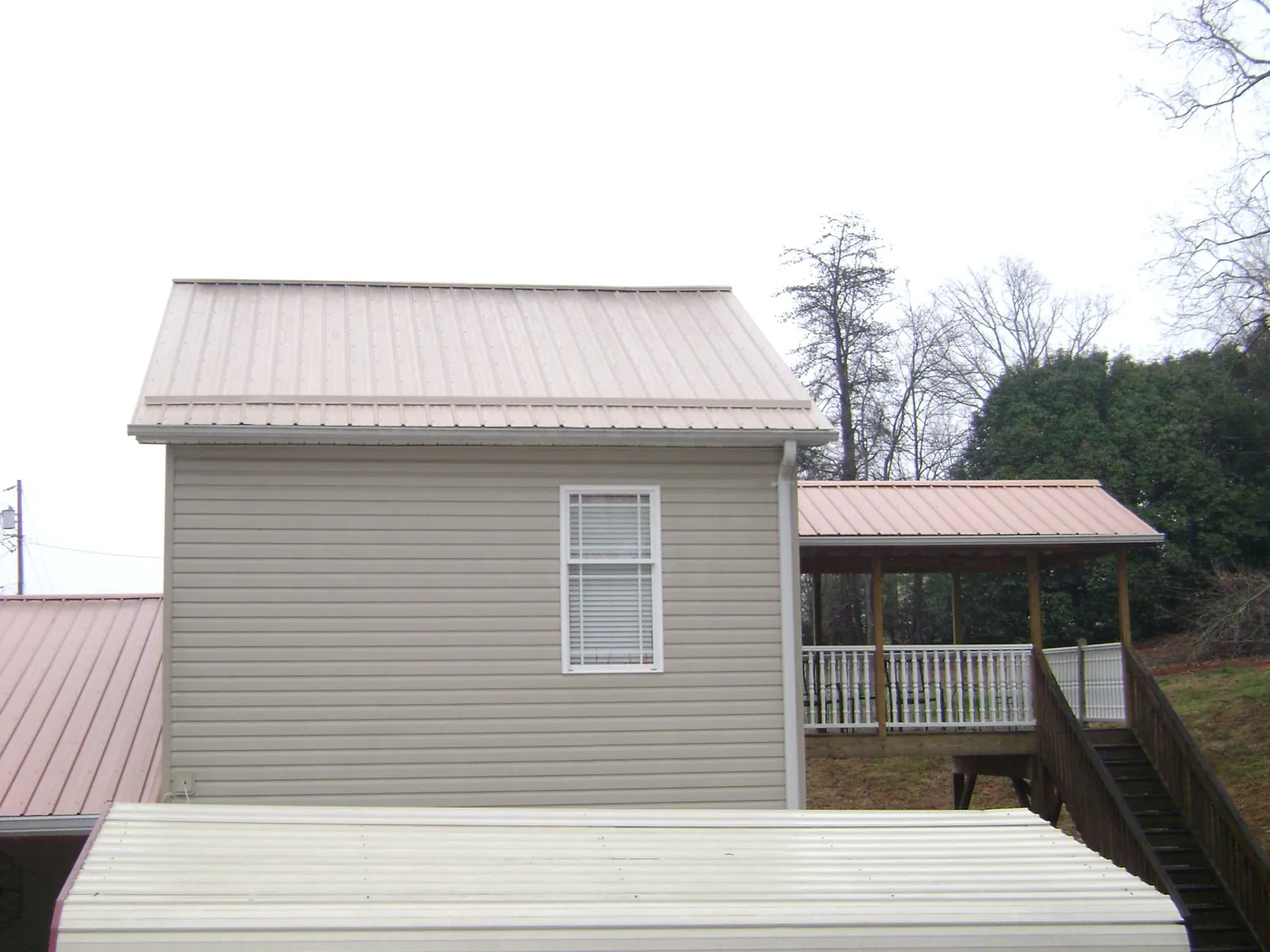 Tan metal roofs on a two story addition and attached porch, from a Roof Replacement job in Mount Aetna